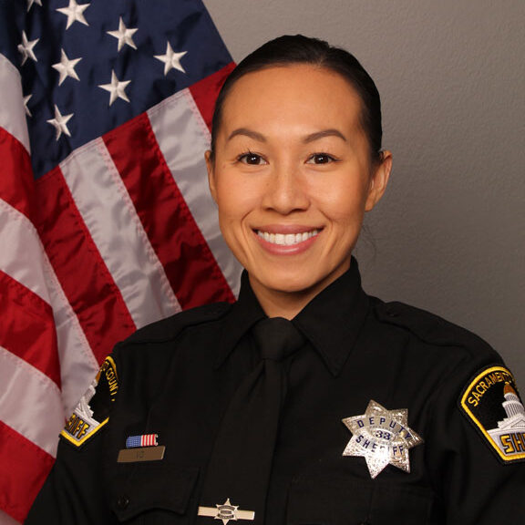 color portrait photograph of Deputy Anna Vo in her Sheriff's uniform with the US flag in the background