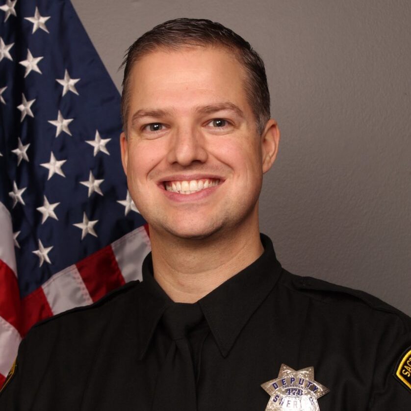 Color portrait photograph of Deputy Jason Jacoby in his uniform with the US flag in the background