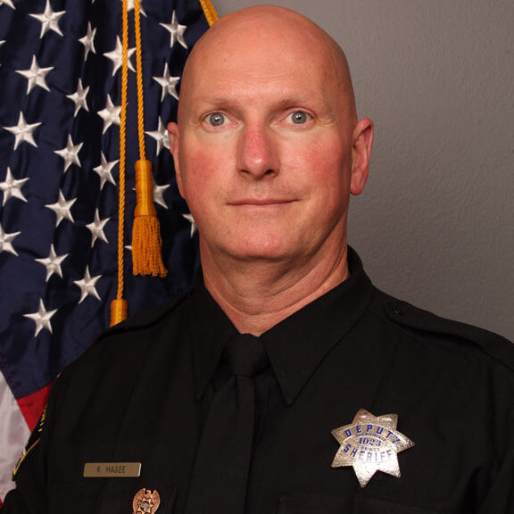 color portrait photograph of Deputy Robert Magee in his Sheriff's uniform with the US flag in the background