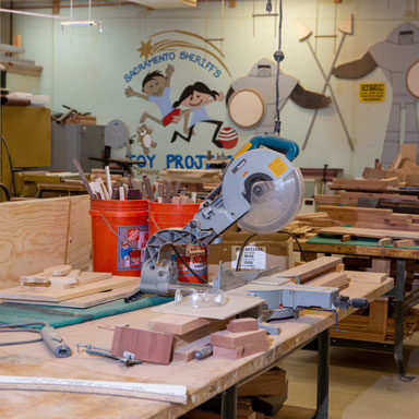 image of the Toy Project Wood Shop showing a radial arm saw, stacks of wood and carpentry tables